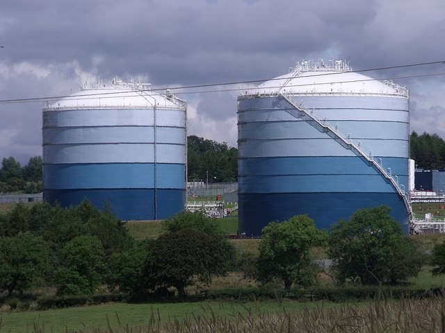 Two large cylindrical natural-gas storage tanks behind a security fence.