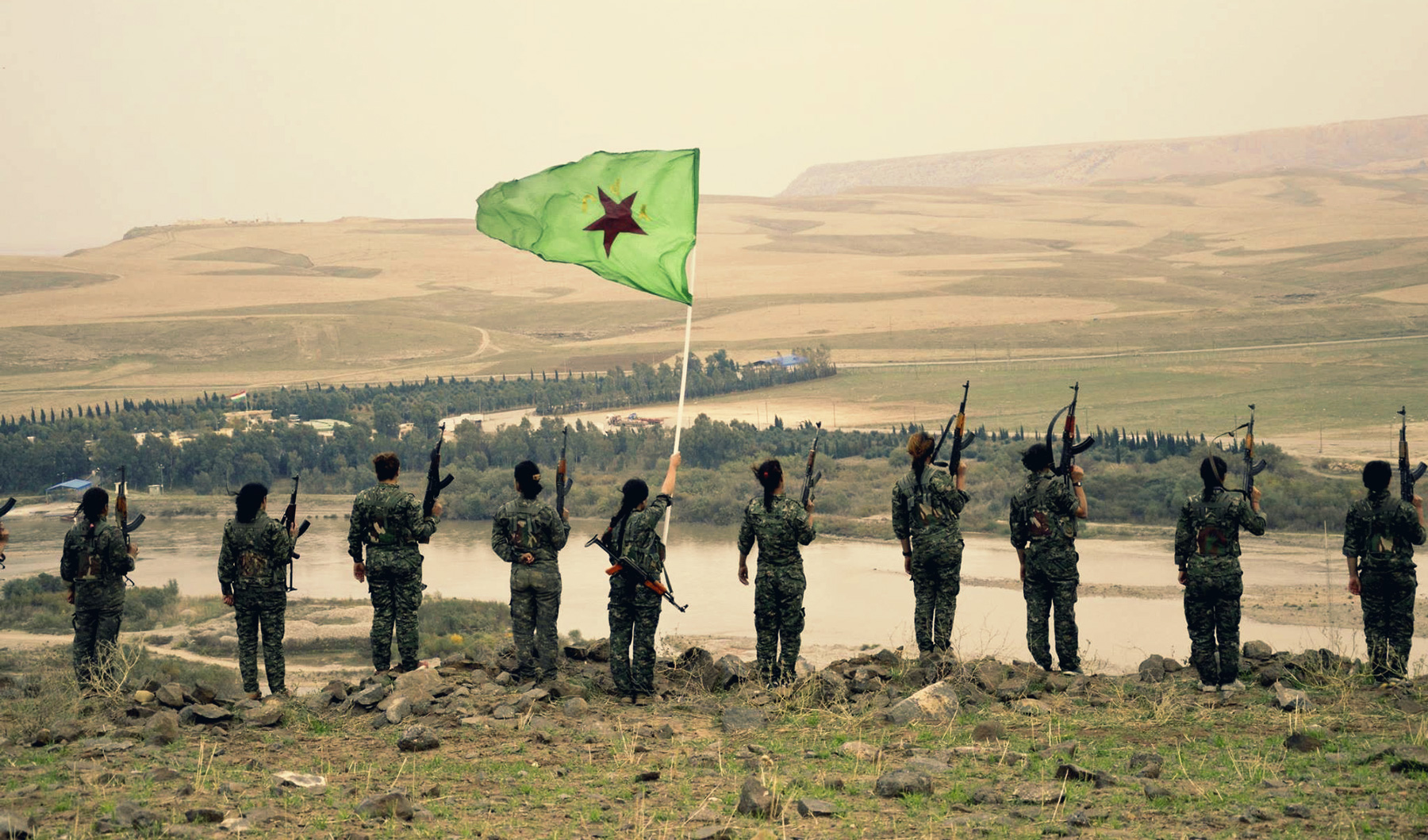 Fighters of the Kurdish women's protection units (YPJ) standing on a hill holding their flag