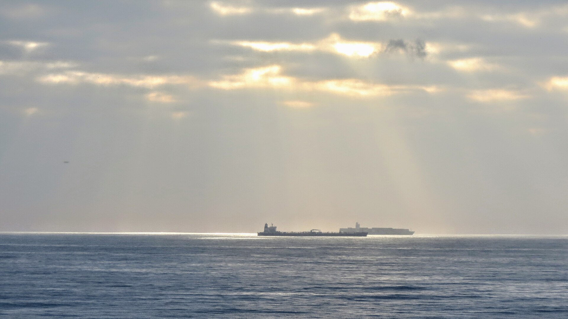 A fully laden crude-oil tanker riding low in the water, waiting at anchor off a harbour.
